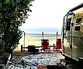 Airstream trailer by ocean with red chairs